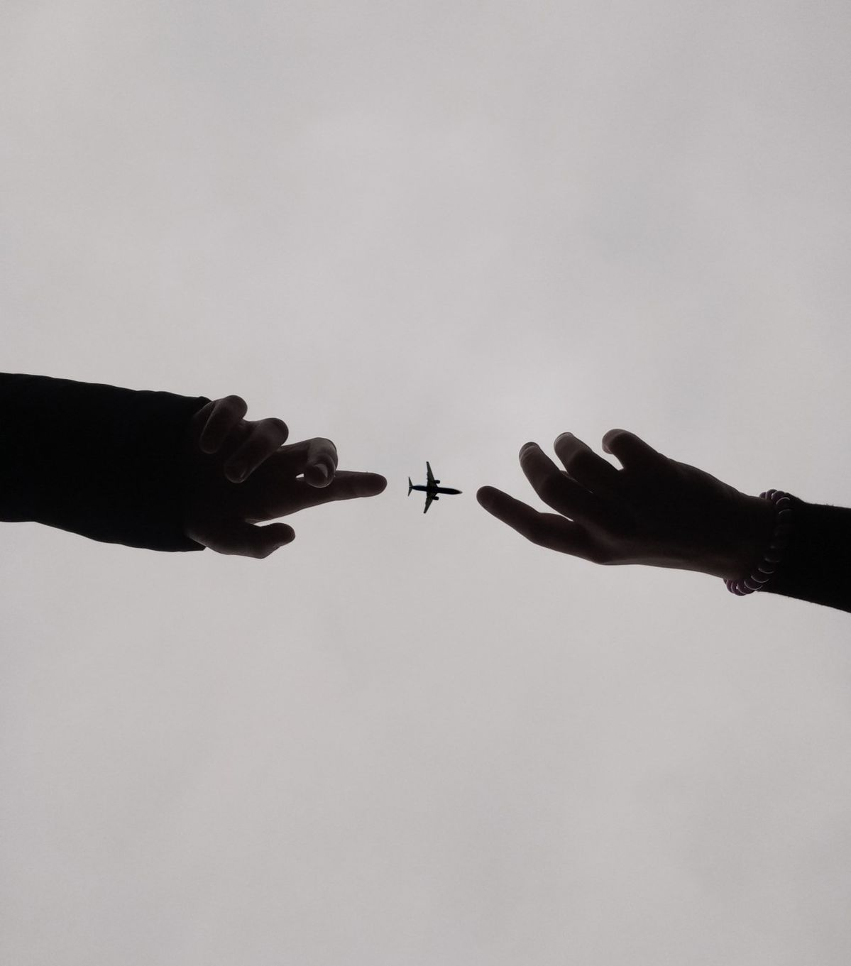 Silhouetted hands reaching toward an aircraft in flight
